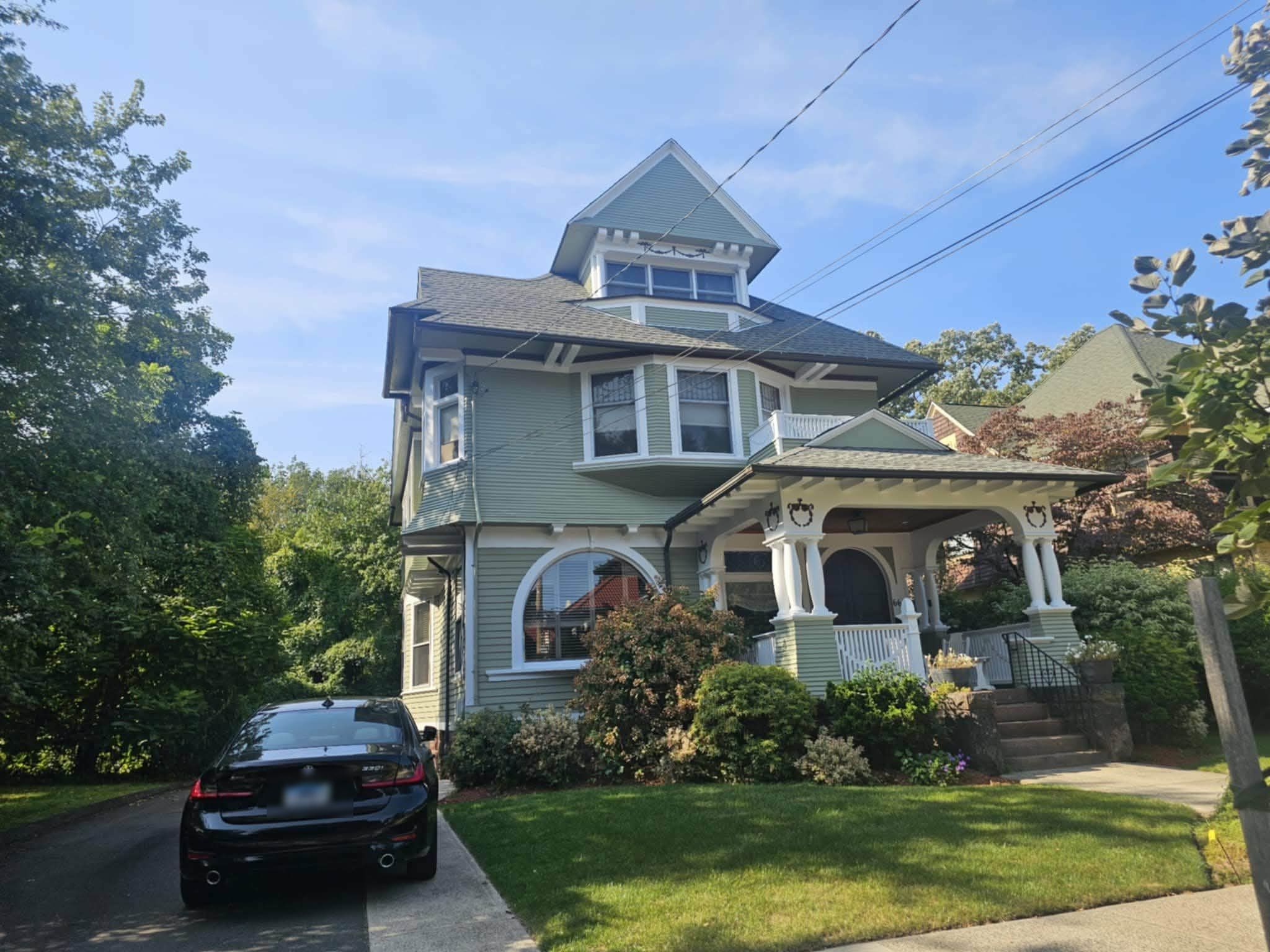 Front of the finished three-story house in sage green with white trim and a wraparound porch