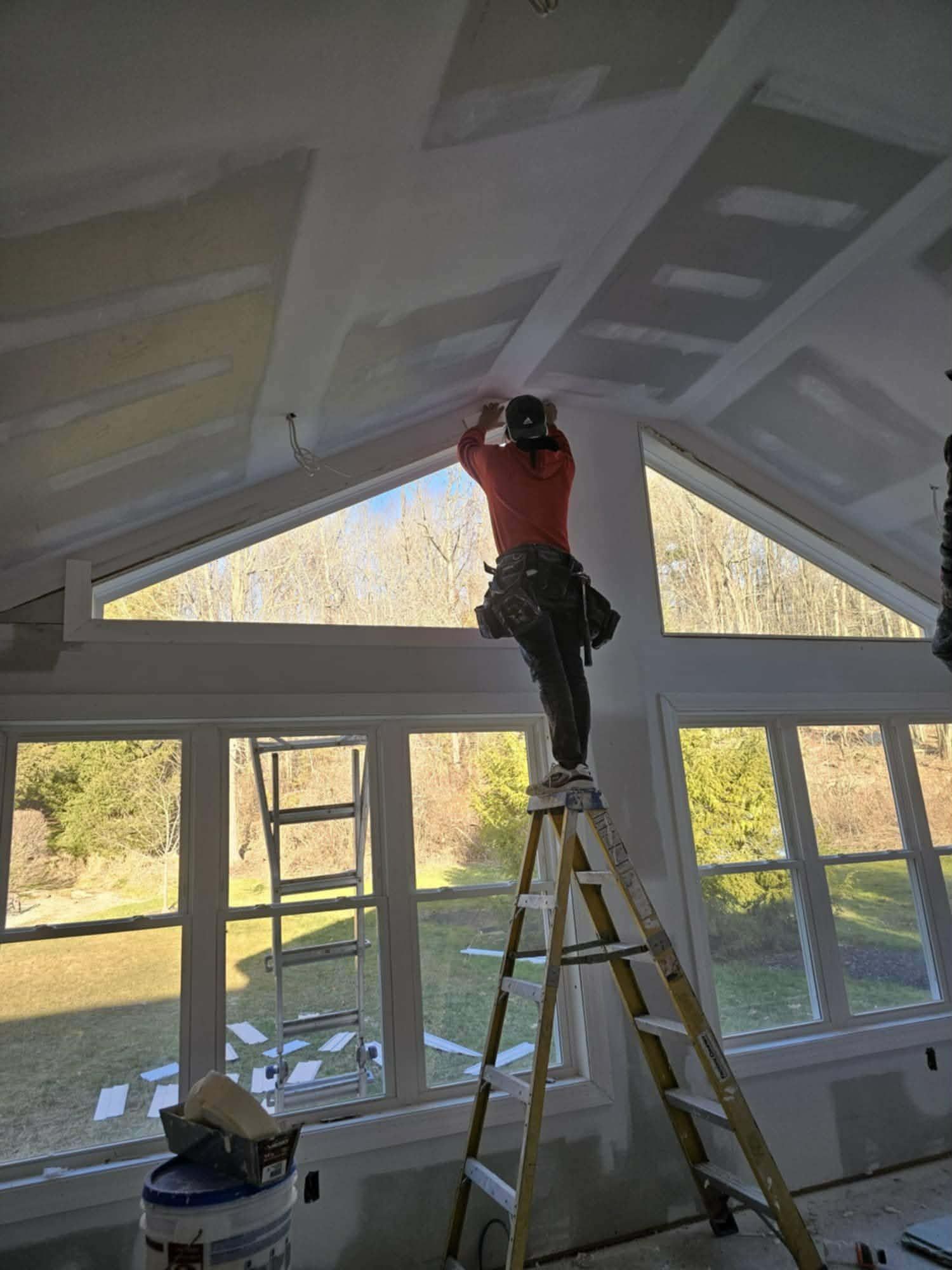 Crew member on a ladder finishing drywall seams under the gable windows