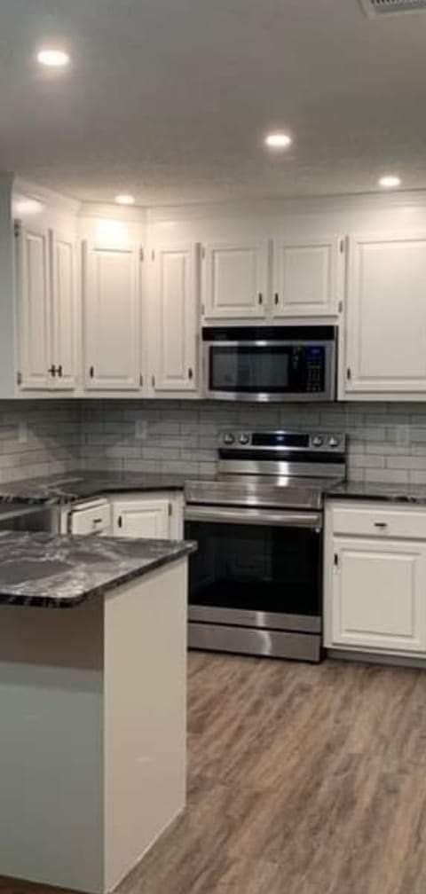 Kitchen with white refinished cabinets, dark granite counters and a stainless range